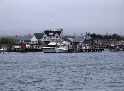 [Several medium size boats as well as smaller one at a doc with multi-level houses peeping over them.]